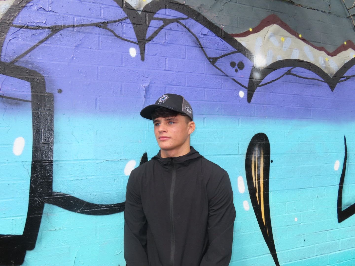 The Iris cap worn against a purple and turquoise street-art wall